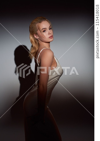 Beautiful young woman in white dress standing under a beam of light 115418018
