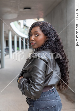 A confident woman is posing outdoors, exhibiting chic style wearing a leather jacket A confident woman is posing outdoors, exhibiting chic style wearing a leather jacket 115418358