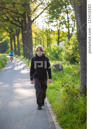 A young man is calmly walking along a forest pathway under the shady trees on a peaceful sunny day 115418383