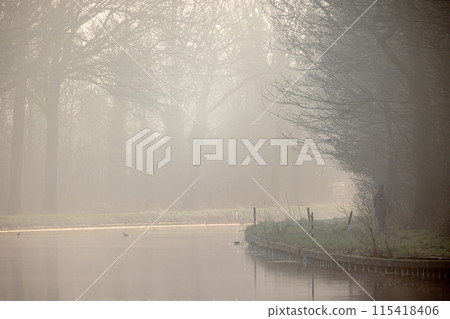 Serene misty morning reflection by the riverbank, surrounded by nature and peaceful ambiance 115418406