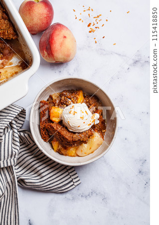 Portion of peach cobbler with scoop of ice cream in bowl, white marble background. 115418850