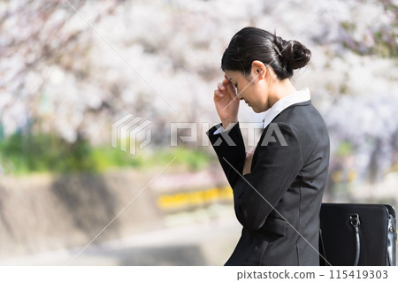 Even though it's spring, a young business woman feels depressed and worried on the riverbank lined with cherry blossom trees. 115419303
