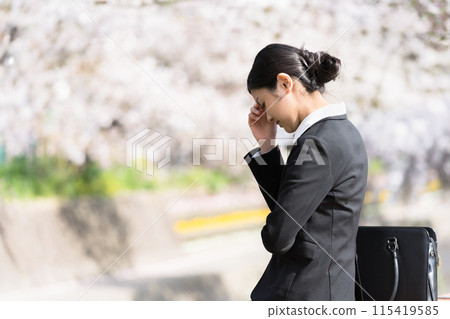 A young business woman who is depressed and worried on the riverbank of a row of cherry blossom trees 115419585