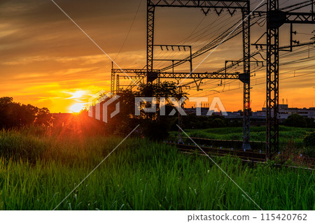 Evening view of the Suzakumon Square at the Heijo-kyo ruins in Nara: The sun sets in the direction of Saidaiji Station, painting the sky and rails golden ① Evening view of the Suzakumon Square at the Heijo-kyo ruins in Nara: The sun sets in the direction of Saidaiji Station, painting the sky and rails golden ① 115420762