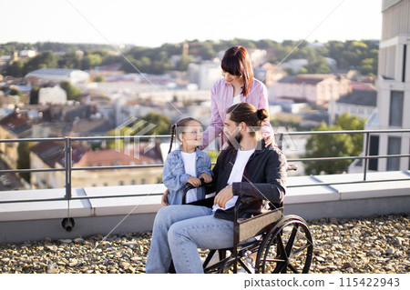 Young man in wheelchair having fun with family on terrace of house. 115422943
