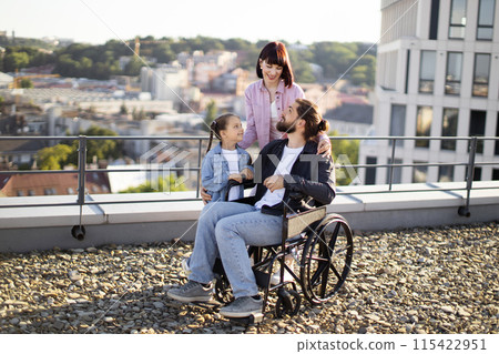 Young man in wheelchair having fun with family on terrace of house. 115422951