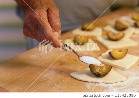 Preparation of homemade fruit dumplings with plums. Czech specialty of sweet good food. Dough on kitchen wooden table with hands. 115423090