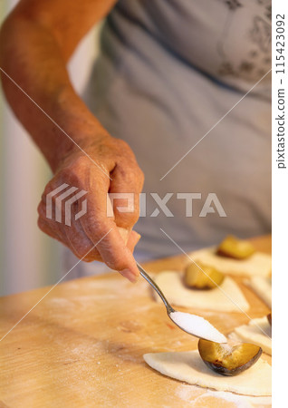 Preparation of homemade fruit dumplings with plums. Czech specialty of sweet good food. Dough on kitchen wooden table with hands. 115423092