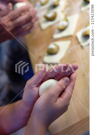 Preparation of homemade fruit dumplings with plums. Czech specialty of sweet good food. Dough on kitchen wooden table with hands. Preparation of homemade fruit dumplings with plums. Czech specialty of sweet good food. Dough on kitchen wooden table with hands. 115423096