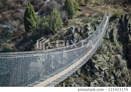 Excursion suspension bridge over the gorge. Sightseeing holiday tour in Kyrgyzstan. Crossing between two mountains Excursion suspension bridge over the gorge. Sightseeing holiday tour in Kyrgyzstan. Crossing between two mountains 115423174