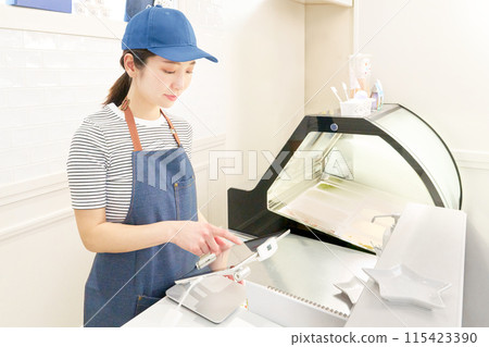 A female store clerk wearing an apron using a tablet register A female store clerk wearing an apron using a tablet register 115423390