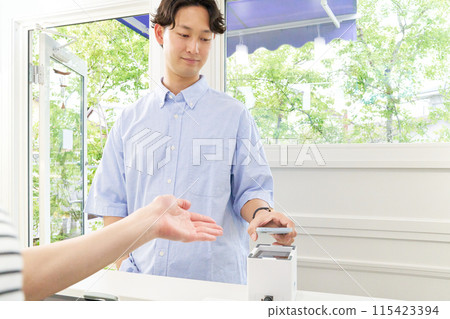 A young male customer making a cashless payment by holding up his smartphone 115423394