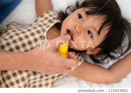 mother or doctor spraying medicine in mouth of toddler. baby sore throat treatment concept mother or doctor spraying medicine in mouth of toddler. baby sore throat treatment concept 115424902