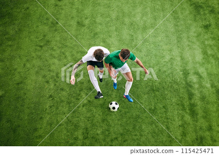 Aerial view. Two players strive to control ball on green lush playground. Sportsmen in comfortable sportswear. Aerial view. Two players strive to control ball on green lush playground. Sportsmen in comfortable sportswear. 115425471