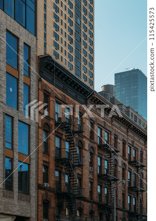 Historic New York City buildings with fire escapes and modern high-rise in background 115425573