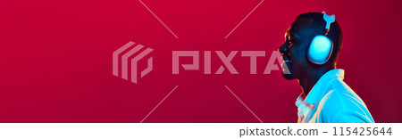 Side view of African-American man listening to music in headphones against red background in neon light 115425644