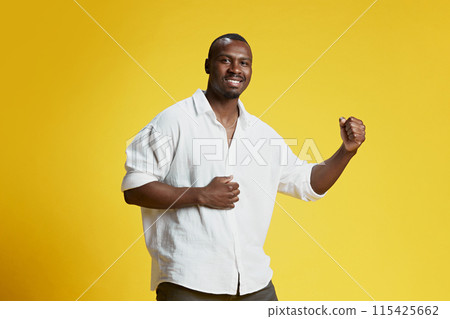 Success and achievements. African-American man in white shirt showing his victory, gesturing against bright yellow background 115425662