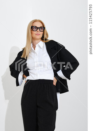 Modern woman in a classic suit holding her hands on her waist and looking into the distance 115425793