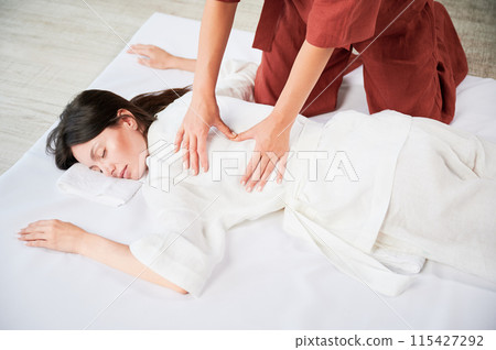 Masseuse making thai yoga massage. Cropped view of woman therapist doing traditional massage treatment for female patient. Client lying on mat, meditating, enjoying hand massage in calm atmosphere. 115427292