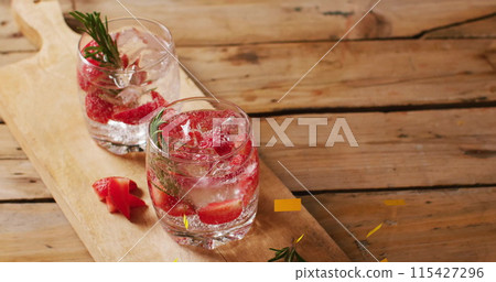 Two refreshing cocktails garnished with rosemary and strawberries on a wooden board 115427296