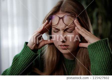 A woman wearing glasses looks uncomfortable and holds her head 115427602