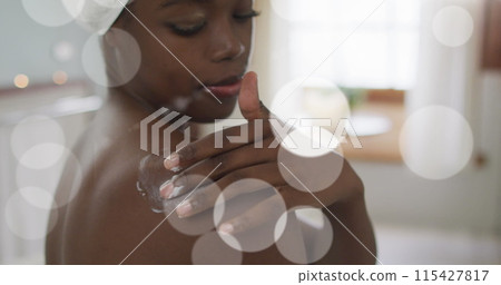 Image of african american woman using cream on body over light spots 115427817