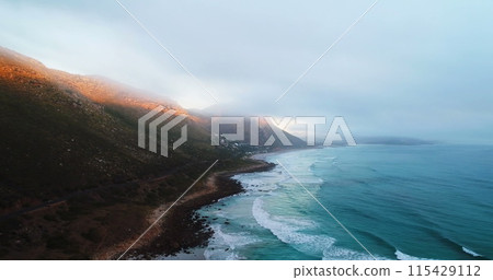 Coastline meets mountain range under a misty sky Coastline meets mountain range under a misty sky 115429112