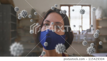 Image of covid 19 cells over woman in pottery studio wearing face mask 115429304