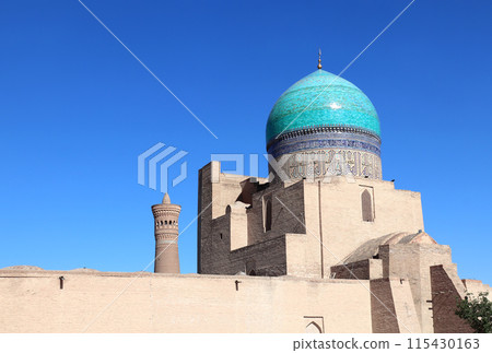 Dome with azure tile of Poi Kalyan Mosque and Kalyan minaret, religious complex of Chor Bakr, Bukhara, Uzbekistan. On blue sky background Dome with azure tile of Poi Kalyan Mosque and Kalyan minaret, religious complex of Chor Bakr, Bukhara, Uzbekistan. On blue sky background 115430163