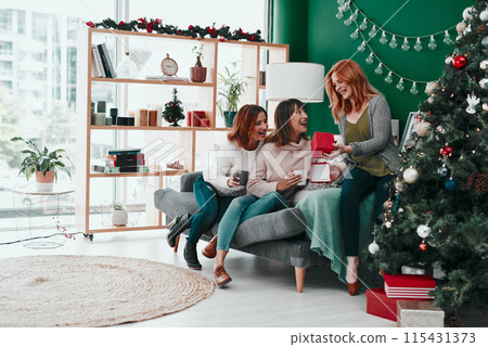 Christmas, group and friends with coffee, gift and happy in vacation of festive season and surprise. Home, lounge and women with open present, warm and smile of girls, together and excited for winter 115431373