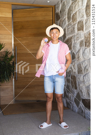 Young Asian man stands at a home entrance, holding a vote badge 115431514