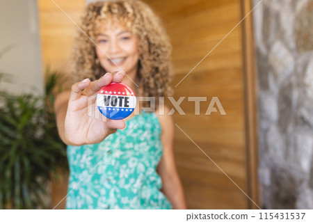 Young biracial woman holds a 'vote' badge towards the camera, with copy space 115431537