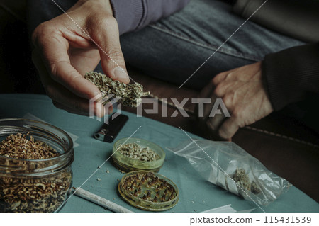 man grinding a cannabis bud with a grinder 115431539