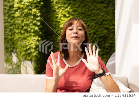 A young biracial woman waves at the camera on a video call A young biracial woman waves at the camera on a video call 115431634