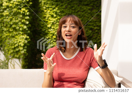 Young biracial woman gestures animatedly outdoors on a video call 115431637