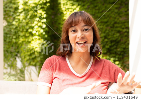 Young biracial woman smiles brightly outdoors on video call Young biracial woman smiles brightly outdoors on video call 115431649