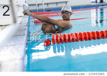 Young biracial male athlete swimmer prepares for a swim at an indoor pool Young biracial male athlete swimmer prepares for a swim at an indoor pool 115431903