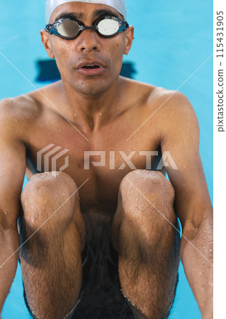 Young biracial male athlete swimmer emerges from a pool, goggle-clad Young biracial male athlete swimmer emerges from a pool, goggle-clad 115431905