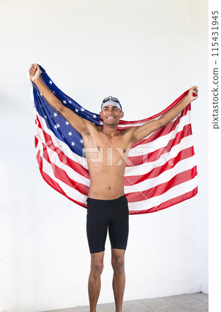 Young biracial male athlete swimmer celebrates victory draped in the American flag 115431945