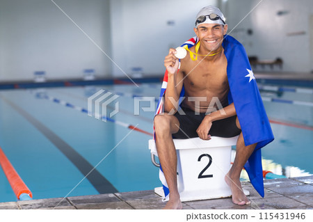 Young biracial male swimmer celebrates at the poolside, draped in an Australia flag with a medal 115431946