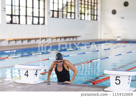 Caucasian female athlete swimmer climbs out of a pool at an indoor facility 115432009