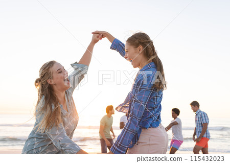 Two young Caucasian women dance on the beach at sunset 115432023