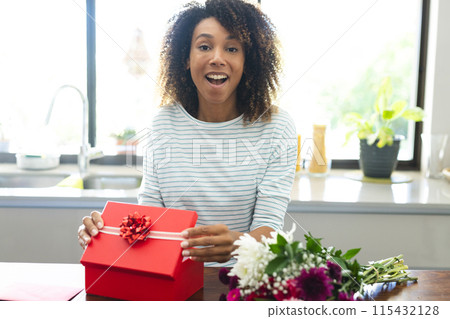Excited biracial woman holding a gift at home during an online date video call Excited biracial woman holding a gift at home during an online date video call 115432128
