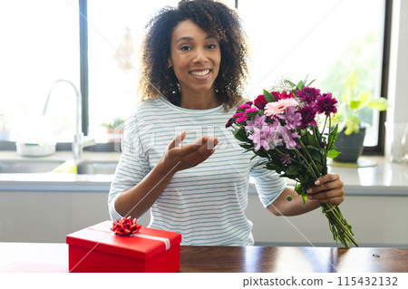 Biracial woman presents a bouquet of flowers at home during an online date video call 115432132