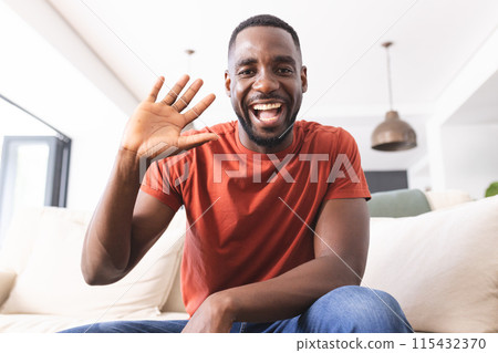 African American man in a red shirt waves with a bright smile on video call African American man in a red shirt waves with a bright smile on video call 115432370