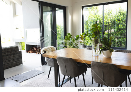 A modern dining room features a large wooden table with grey chairs and a fireplace, with copy space A modern dining room features a large wooden table with grey chairs and a fireplace, with copy space 115432414
