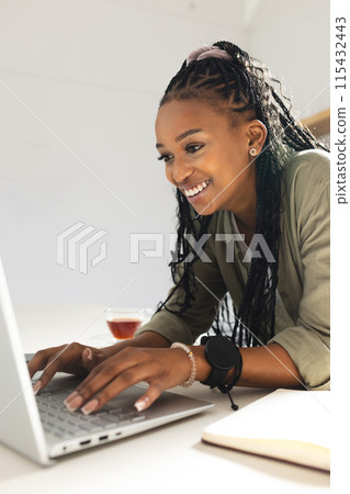 A young African American woman smiles while using a laptop A young African American woman smiles while using a laptop 115432443