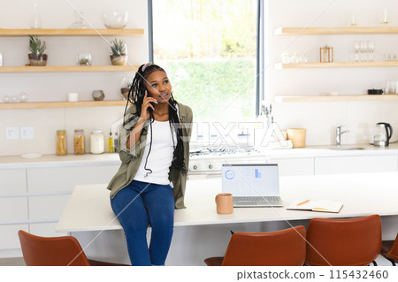 A young African American woman chats on the phone, leaning on a kitchen island with copy space A young African American woman chats on the phone, leaning on a kitchen island with copy space 115432460