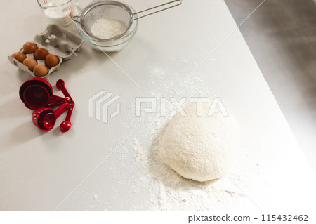 A mound of flour with dough sits on a kitchen counter with copy space, surrounded by baking ingredie 115432462