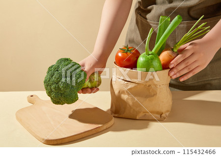 Kitchen background photo from front angle shot, a chef putting a green cabbage on a wooden chopping board, which placed on a table next to a bag of vegetable. Blank space for advertising Kitchen background photo from front angle shot, a chef putting a green cabbage on a wooden chopping board, which placed on a table next to a bag of vegetable. Blank space for advertising 115432466